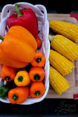 colorful peppers and jalapeño in white glass basket with corn on the cob sitting on a cutting board