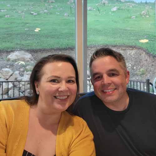 amy-and-mike-cross-in-their-airbnb-with-beautiful-green-grass-out-the-window-behind-them