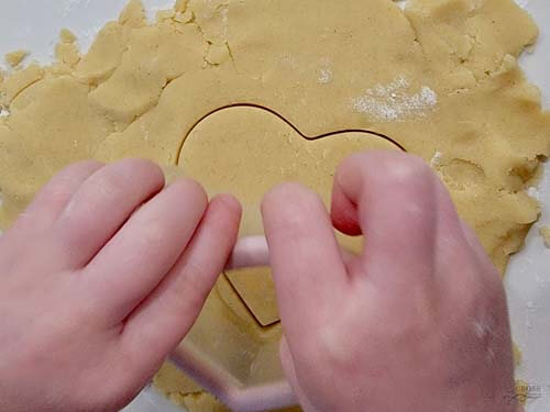 a baker in the making helping to peel the surrounding dough from the cookies