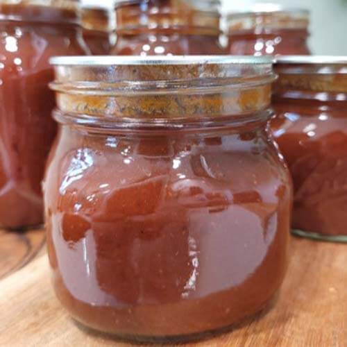 close-up-of-bbq-sauce-in-glass-mason-jars-sitting-on-a-wooden-cutting-board