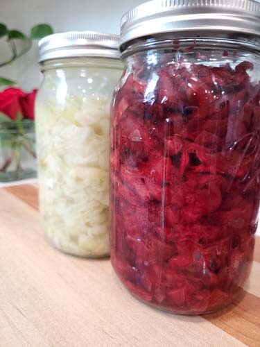 red-and-white-homemade-sauerkraut-in-mason-jars-sitting-on-a-wooden-cutting-board
