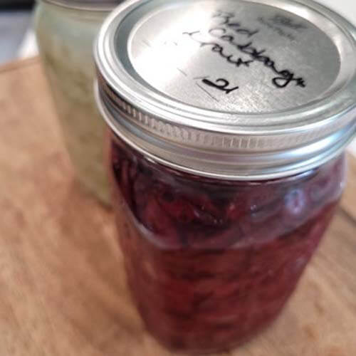 two-pint-size-jars-of-sauerkraut-sitting-on-a-wooden-cutting-board