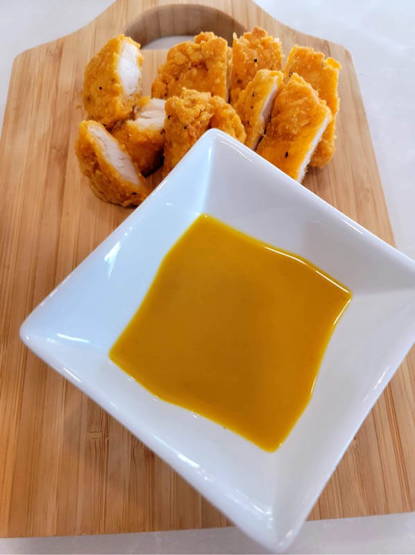chopped-chicken-strips-on-a-wooden-cutting-board-with-honey-mustard-dressing-in-a-square-white-sauce-dish