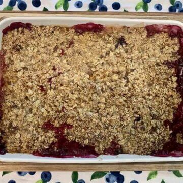 fully cooked Peach Blueberry Crisp in a white baking dish cooling on a wooden cutting board