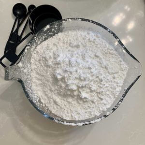 Homemade Monk Fruit Powdered Sugar in a glass bowl with black measuring cups