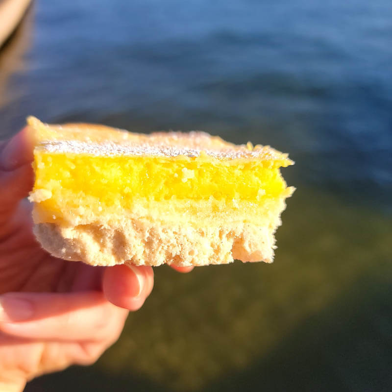Amy holding a slice of lemon bar with the lake in the background