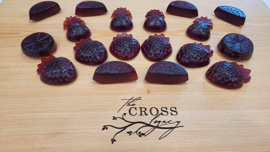 strawberry shaped elderberry gummies sitting on a wooden cutting board with The Cross Legacy logo engraved on it