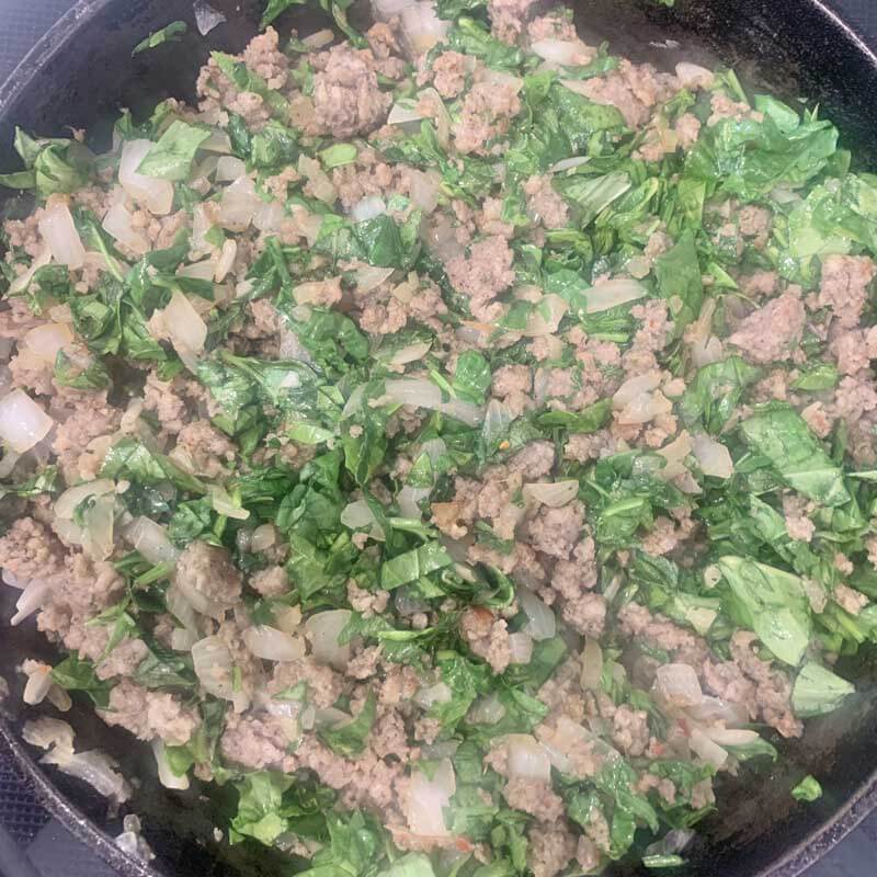 Sausage, chopped spinach, and onion in a pan.